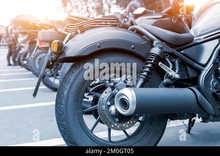 Vista dettagliata ravvicinata del disco silenziatore del tubo di scarico della ruota posteriore del motociclo del trinciatore classico parcheggiato in city Street. Molte moto sul parcheggio della strada cittadina Foto Stock