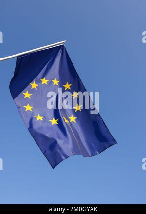 Bandiera dell'Unione europea appesa a flagstaff sopra il cielo azzurro, simbolo del patriottismo europeo, angolo basso, vista laterale Foto Stock