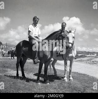 1950s, storico, giro di vacanza, due uomini a cavallo su un terreno sabbioso e erboso su una costa, Inghilterra, Regno Unito. Foto Stock