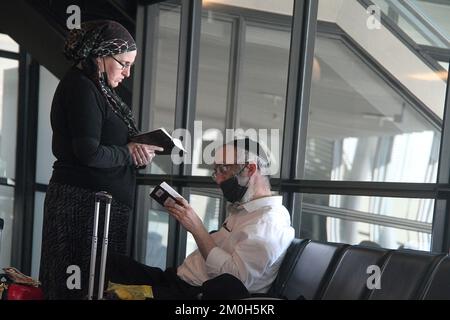 Una coppia ebraica che legge mentre scrive nel terminal di un aeroporto internazionale Foto Stock