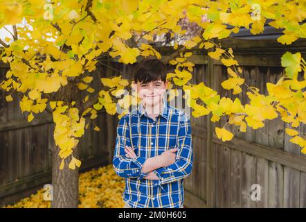 Ritratto di ragazzo in piedi accanto a foglie di albero gialle il giorno di autunno. Foto Stock
