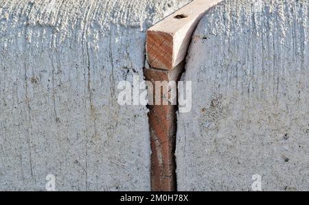 Giunti di dilatazione con distanziatori in legno che separano le sezioni in calcestruzzo di un cordolo per assorbire le sollecitazioni derivanti dall'espansione indotta dal calore. Immagine di primo piano a livello del suolo. Foto Stock