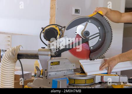 Su una sega circolare, l'operaio di costruzione taglia i pannelli di modanature di legno come parte del lavoro di finitura Foto Stock