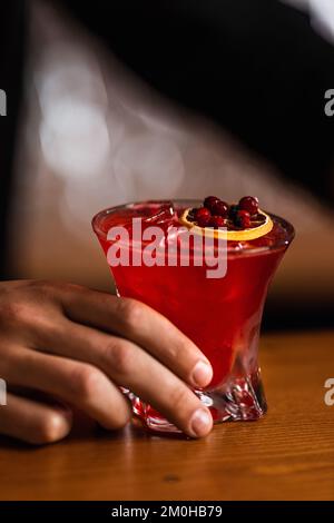 Deliziate il cocktail di mirtilli rossi con cubetti di ghiaccio. Il barman esperto crea un cocktail di mirtilli al bar. Bevanda alcolica rossa. Foto Stock