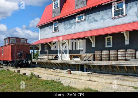 Una fila di vecchie botti di legno su un molo della stazione ferroviaria con un caboose rosso Foto Stock