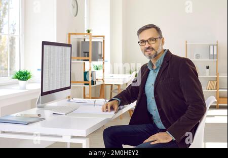 Uomo d'affari o contabile finanziario seduto alla sua scrivania con un computer desktop Foto Stock