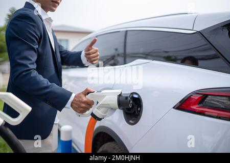 Giovane uomo d'affari che tiene un caricabatterie per veicoli elettrici Foto Stock