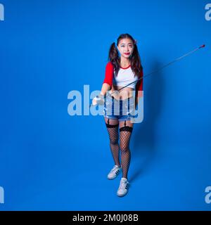 Giovane donna in Harlequin Costume Holding Fencing foil contro uno sfondo blu solido Foto Stock