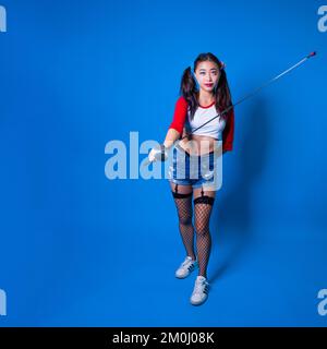 Giovane donna in Harlequin Costume Holding Fencing foil contro uno sfondo blu solido Foto Stock