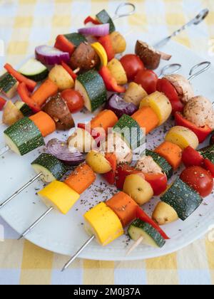 Spiedini con verdure miste (zucchine, patate, carote, peperone, funghi) su un piatto, pronti per essere grigliati. Foto Stock