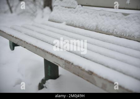 Primo piano di bianche panchine in legno innevate in un parco. Foto Stock