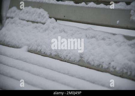 Primo piano di bianche panchine in legno innevate in un parco. Foto Stock