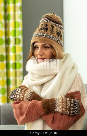 Una giovane donna seduta su un divano che indossa un cappello, una sciarpa e dei guanti di lana Foto Stock