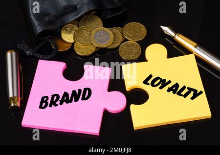 Concetto di business e finanza. Le monete sono sparse sulla superficie nera, ci è una penna ed i puzzle su cui è scritto - LEALTÀ DI MARCA Foto Stock