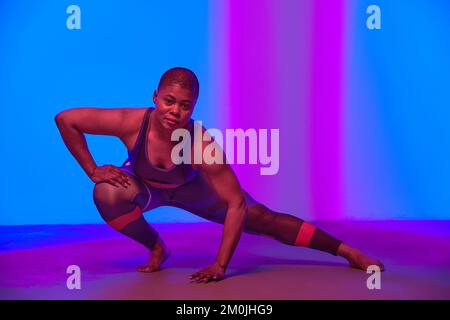 Attività fisica. Intera lunghezza verticale Ritratto del corpo positivo giovane donna nera in sport Top Bra e leggings posa in studio guardando la fotocamera Foto Stock