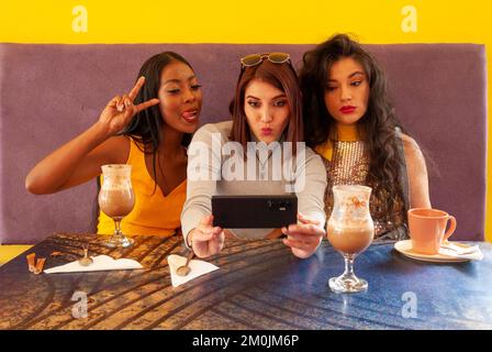 Un gruppo di tre amici femminili in un bar che scattano selfie e si divertono Foto Stock