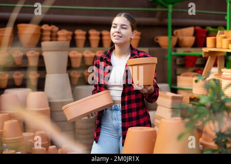 Ragazza giovane che sceglie le pentole per le piante domestiche crescenti nel deposito di giardinaggio Foto Stock
