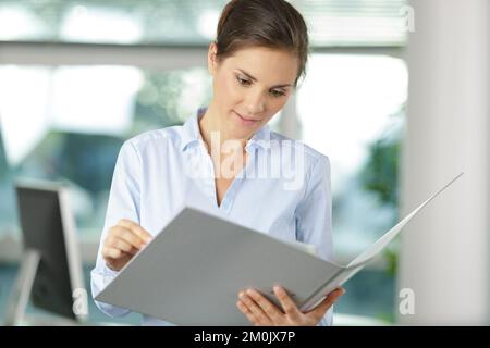 donna in ufficio con una maglietta bianca che contiene la cartella dei documenti Foto Stock