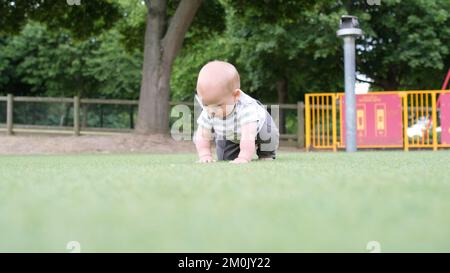 Buona famiglia che ha picnic. Il bambino piccolo sta strisciando sull'erba verde. Estate nel parco. Fratelli bambini che giocano nel parco verde. Divertimento e gioia per tutta la famiglia Foto Stock