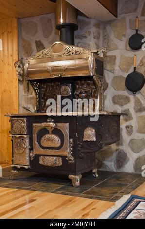 Antica stufa in ghisa in legno nel seminterrato camera familiare all'interno 1978 costruito replica di vecchio canadiana cottage stile log e fieldstone casa. Foto Stock