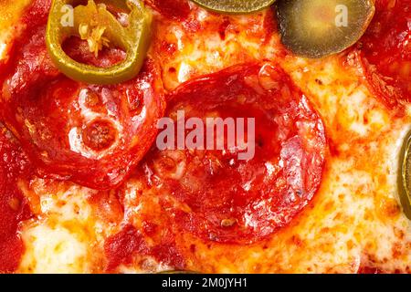 Pasta di pizza al peperoni salame con jalapeno come sfondo. Un bicchierino di pizza. Foto macro. Pizza con salame di peperoni e jalapenos. Foto Stock