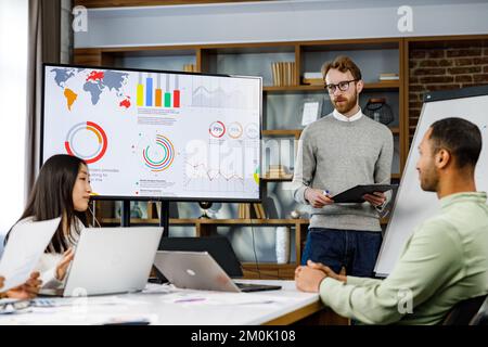 Team leader motivato che spiega la strategia di sviluppo aziendale ai giovani colleghi multinazionali sorridenti. Felice gente di affari multirazziale godere Foto Stock