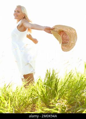 Amare la libertà dell'estate. Una giovane donna in un campo che tiene un cappello da sole. Foto Stock