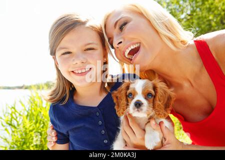 Mamme il meglio. Ritratto di una bambina che tiene un cucciolo mentre sua madre sorride a lei amorevolmente. Foto Stock