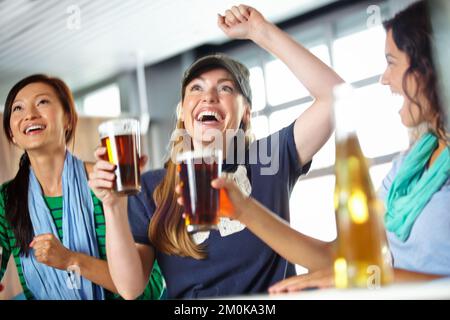 Sport e bere rendono la sua vita incredibile. Tre amiche che si tirano indietro con qualche drink al bar e guardano lo sport. Foto Stock