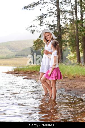 Legame fuori in natura. Una bambina carina che tiene la madre per mano mentre sta in piedi in un ruscello selvaggio. Foto Stock