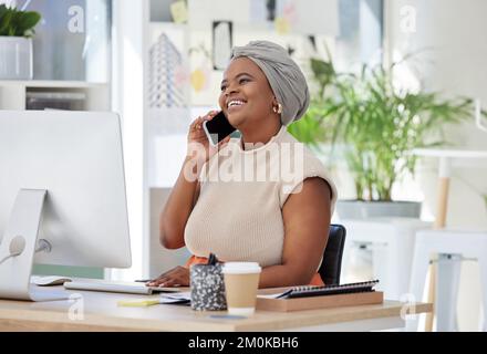 Giovane donna d'affari afroamericana seduta da sola in un ufficio e che parla con i clienti con un cellulare. Sorridente ambizioso nero creativo professionale Foto Stock