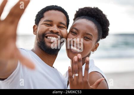 Ritratto di una coppia afro-americana che prende un selfie mentre mostra un anello al mare insieme. Felice ragazzo e ragazza dopo aver scattato una foto Foto Stock