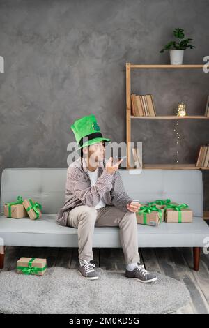 Uomo in leprechaun cappello che tiene uno smartphone parlare con un assistente digitale o un amico usa a distanza la messaggistica vocale facile il giorno di San Patrizio. concetto di Foto Stock