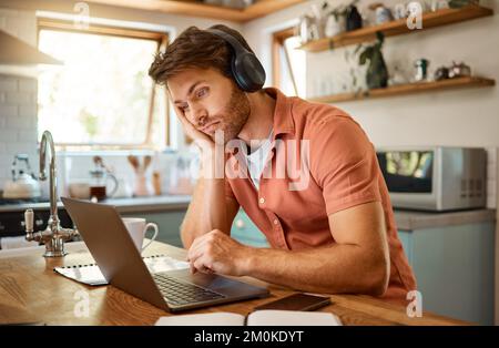 Giovane uomo d'affari caucasico serio che indossa cuffie e ascolta musica mentre lavora su un computer portatile da sola. Un uomo d'affari stressato Foto Stock