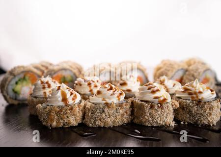 Set caldo sushi panini fritti crema di formaggio decorato. Assortimento di deliziose tempura e maki di sushi al forno con salmone. Vulcano sushi su sfondo bianco. Foto Stock