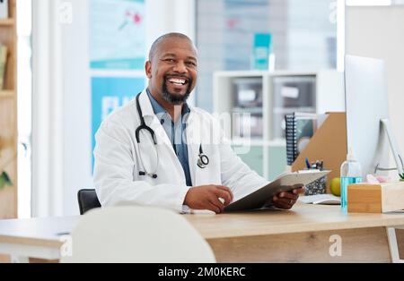 Bel medico nel suo ufficio. Medico afro-americano che legge una tabella dei pazienti. Professionista medico maturo che legge le informazioni del paziente. Medico Foto Stock