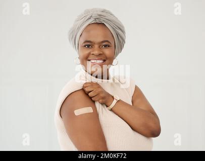 Donna afro-americana matura che indossa e mostra un bandaid sul braccio in piedi contro uno sfondo bianco studio. Donna matura che mostra un cerotto su Foto Stock