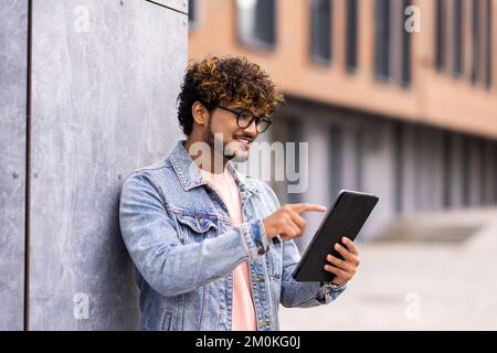 Bell'uomo che usa il tablet digitale in una città. Studenti che leggono all'aperto. Foto Stock
