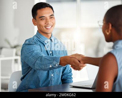 Due uomini d'affari allegri che scuotono le mani in un'intervista insieme al lavoro. Colleghi felici salutano con una stretta di mano in un ufficio. Capo maschio asiatico Foto Stock