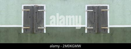 Due vecchie finestre con persiane chiuse in una facciata verde e bianca Foto Stock