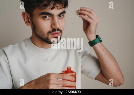 Ritratto bell'uomo che tiene una bottiglia di vetro con l'olio di siero medicinale. Lifestyle people, maschio personale auto cura, prodotti, accessori. Foto Stock