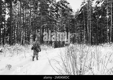 American Medic Soldier of USA Fanteria della seconda guerra mondiale Marching lungo Forest Road in Winter Day. Foto a colori in bianco e nero Foto Stock