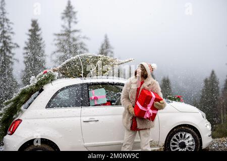 La donna viaggia in auto con regali e albero di Natale sulla strada di montagna Foto Stock