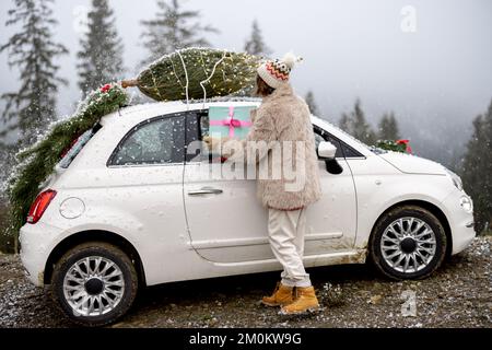 La donna viaggia in auto con regali e albero di Natale sulla strada di montagna Foto Stock