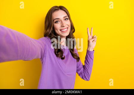 Selfie primo piano cadre foto di giovane attraente influencer signora prendere scatto mostrando segno V amichevole persona sorridente isolato su sfondo giallo colore Foto Stock