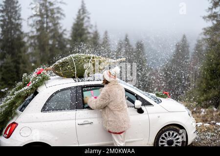 La donna viaggia in auto con regali e albero di Natale sulla strada di montagna Foto Stock