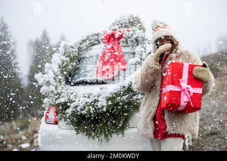 La donna viaggia in auto con regali e corona di Natale sulla strada di montagna Foto Stock