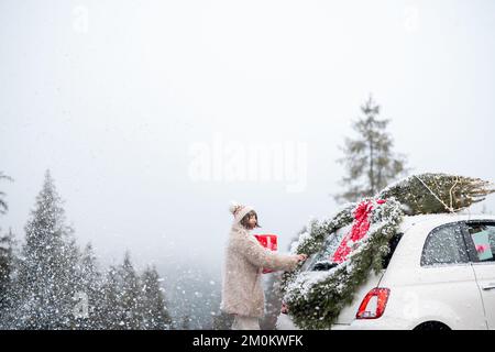 La donna viaggia in auto con regali e albero di Natale sulla strada di montagna Foto Stock