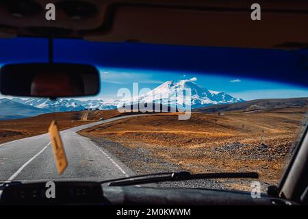 Una strada asfaltata tortuosa in zona montagnosa. Una strada pittoresca sulle montagne del Caucaso settentrionale. Vista del Monte Elbrus dall'auto Foto Stock