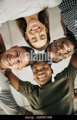 Il team di creativi si è riunito in un'unità. Felice team di business diversificato in piedi in cerchio abbracciando l'un l'altro e sorridendo, dal basso Foto Stock